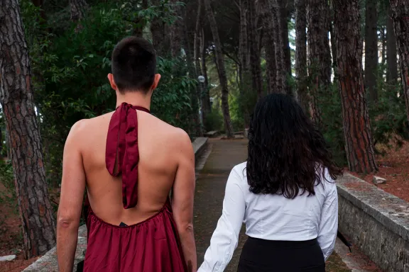 uomo di spalle che indossa un abito femminile e tiene per mano una donna