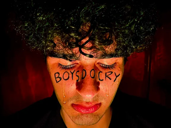 ragazzo in lacrime con la scritta "boys do cry" sul viso