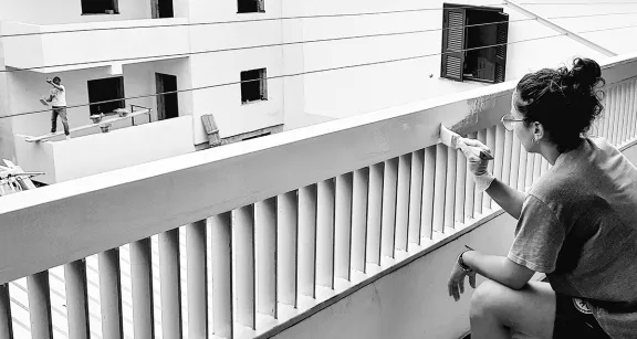 giovane donna che ridipinge un balcone e operario sullo sfondo intento nella medesima attivit&agrave;